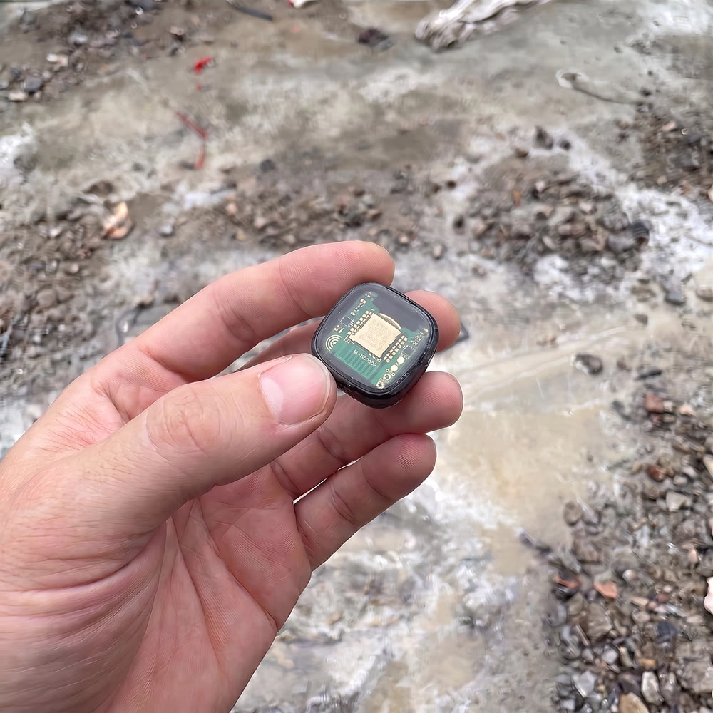 A Safecrete Qube maturity sensor held in hand at a shotcrete face, its epoxy-encased circuit board and antenna visible